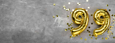 Yellow foil balloon number ninety nine on a concrete background. Greeting card with the inscription 99. Anniversary concept. for anniversary, birthday, new year celebration. banner,の写真素材
