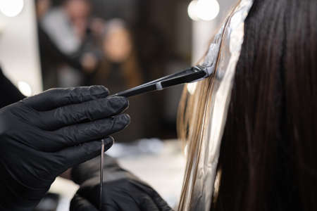 close-up side view of a strand of female hair on a special sheet of foil, the master applies hair dye with a brush. The process of highlighting by a professional master in a beauty salon. lifestyleの写真素材