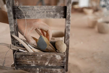 close-up modeling tools in a wooden box. Pottery, ceramic art concept. female hand takes a paint sponge for applying paintの写真素材