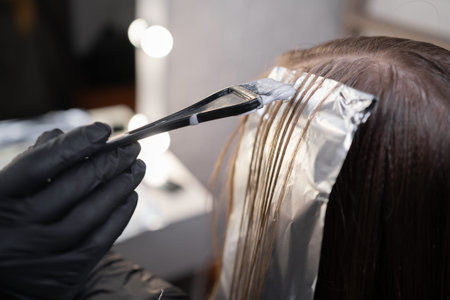 Close-up of a strand of female hair on a special sheet of foil, the master applies hair dye with a...