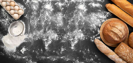 Bakery products golden rustic bread crusts and buns on a black board background eggs sieve and flour. Still life captured from above banner. copyspace.の写真素材
