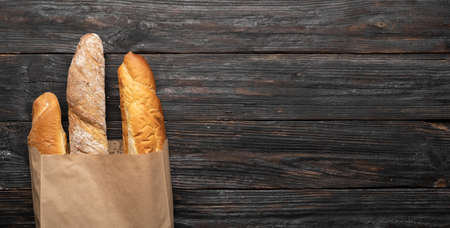 Three crispy french baguettes on a wooden background in a paper bag. view from above. copyspace. bannerの写真素材