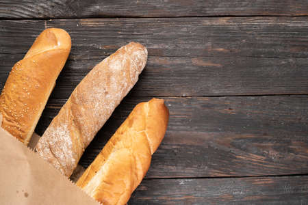Three crispy french baguettes on a wooden background in a paper bag. view from above. Copy space, flat lay.の写真素材