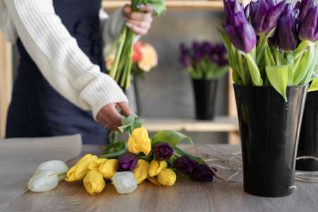 Woman florist creates a bouquet of yellow tulips. Close-up of the masters hands in the workshop take a bouquet.の写真素材