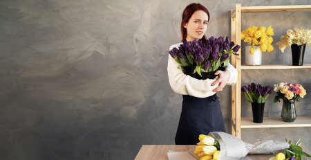 Young female florist at work. Business woman and floristry sale concept happy smiling woman making tulip bouquet in flower shop. Beautiful florist girl with flowers. banner.の写真素材