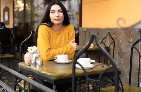 Relaxation in autumn in a street cafe, brunette woman drinking coffee and daydreaming, lunch breakの写真素材