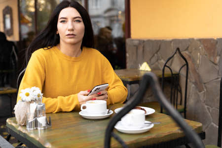 Young woman freelancer with smartphone sitting in street cafe with coffee. Conceptual meeting, work online, freelancingの写真素材