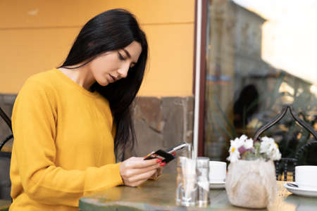 Buying online, paying for an order with a credit card, a brunette woman making an online purchase using a card and a mobile phone, a visitor to a street cafe, a smartphone userの写真素材
