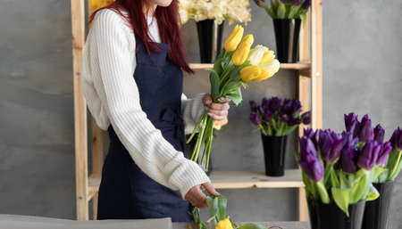 Woman florist creates a bouquet of yellow tulips. Close-up of the masters hands in the workshop take a bouquet.の写真素材