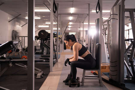 rest and relaxation after training. young caucasian woman sitting in the gym taking a break between exercises.の写真素材