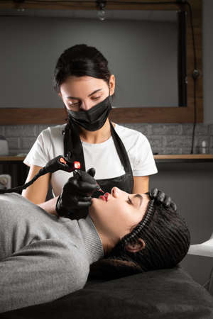 Permanent makeup. Spa beauty treatments. young woman. the master puts the tattoo on the lips. Professional facial microblading. Female cosmetology apparatus.の写真素材
