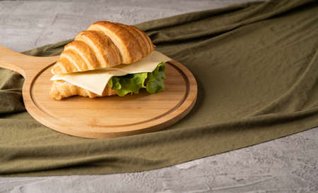 Breakfast croissant sandwich with ham and cheese on a round board.の写真素材
