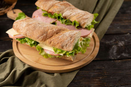 Two fresh sandwiches with ham, cheese, lettuce, on a wooden cutting board.の写真素材