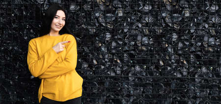 Brunette woman isolated on black structural background, 30s girl with long hair standing near a wall made of lattice and large black stone, bannerの写真素材