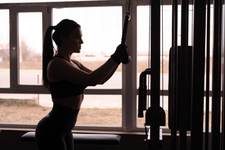 Woman training triceps. A young attractive woman with a perfect body is doing exercises on a cable...