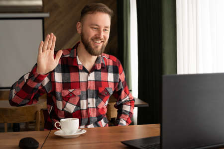 Smiling millennial Caucasian casual man, smiling while working with apps, guy chatting online on laptop, sitting at table in cafe, happy 30 year old businessman using wi-fi in public placeの写真素材