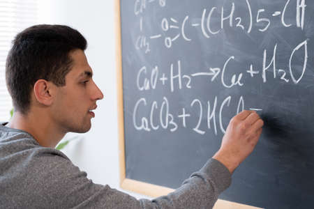 Arabic student at university chemistry lesson writing formulas on blackboard, education and science chemistry, organic science conceptの写真素材