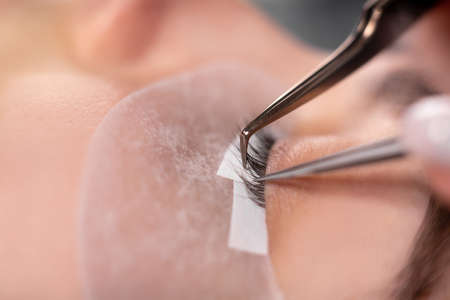 eyelash extension procedure master tool close-up. long eyelashes. A beautiful girl is lying on a sofa in the eyelash master's office.の写真素材