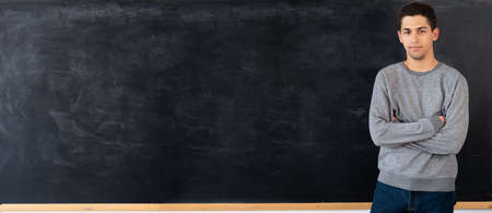 Thoughtful young arabic man standing next to empty chalk board at school or university, young male on blackboard background, knowledge concept, layout, bannerの写真素材
