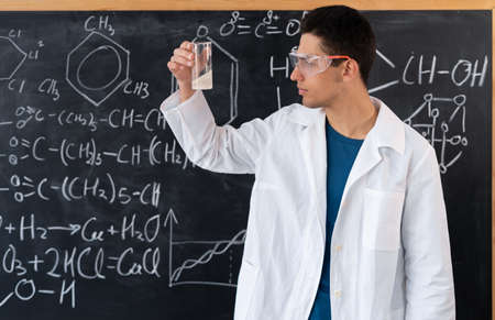 Science chemistry, university lab assistant doing chemistry experiment with liquids in flask, young arabic student doing acid mixing experiment, university education conceptの写真素材