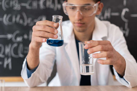 portrait of an arabic chemist conducting an experiment on mixing liquids in a flask, a laboratory assistant in glasses shows a chemical reaction in a lesson, education conceptの写真素材