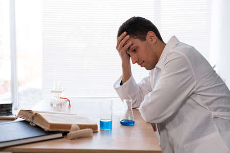 Stressed out scientist researcher feeling tired while worrying about a problem in chemistry lab. Young arab studying chemistry in a laboratory room, school chemistry teacher, results of the experimentの写真素材