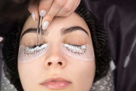 Eyelash extension procedure. The master with tweezers forges long eyelashes to beautiful female eyes. the master makes a marking with a marker.の写真素材