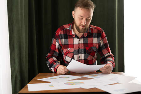 Serious thoughtful businessman looking at papers while sitting at table and working at home or office interior. Business or freelancing concept.の写真素材