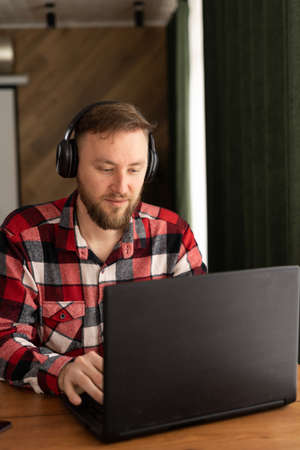 Happy caucasian millennial male working on laptop with headphones while sitting at workplace in modern office. business and entrepreneurship. Successful career and remote work conceptの写真素材