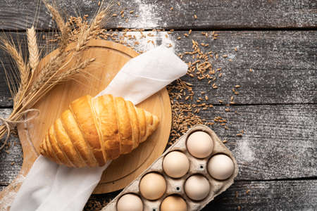 Freshly baked croissant in a bakery on a wooden background with eggs, pastry shop food, bread and roll production concept, top view, flat lay, space for textの写真素材