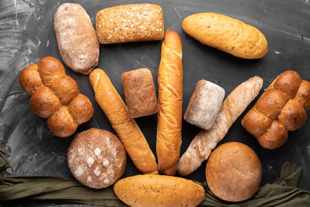a lot of fresh bread on a black background, top view. Homemade fresh pastries of various loaves of wheat and rye bread close-up. copyspace.の写真素材