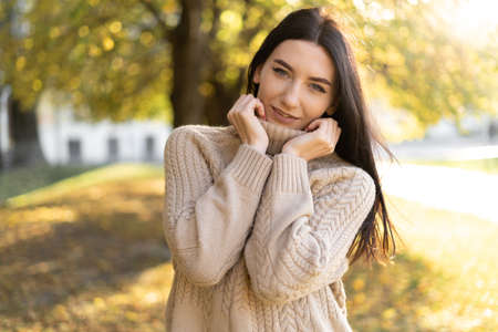 autumn portrait of a young brunette outdoors, a girl in a park among the foliage wrapped in a sweater, the concept of a walk in natureの写真素材