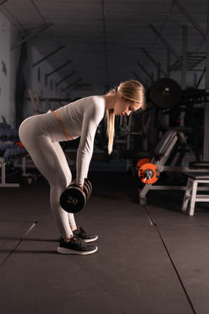 young caucasian girl in the gym doing an exercise for the back with dumbbells deadlift. copyspace.の写真素材