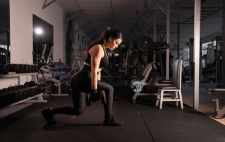 Fitness woman doing lunge exercises with dumbbells in her hands to train leg muscles in the gym. Active girl squats on one leg.の写真素材