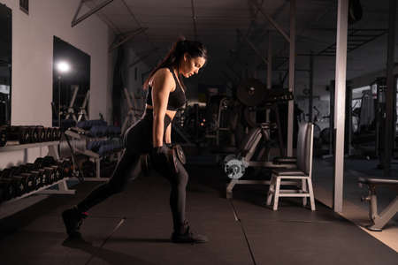 Fitness woman doing lunge exercises with dumbbells in her hands to train leg muscles in the gym. Active girl squats on one leg.の写真素材