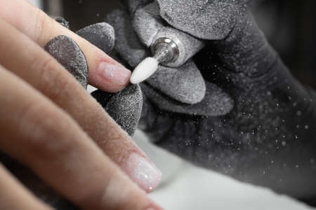 Manicurist uses an electric drill to remove old gel polish from nails. A woman is getting a manicure of nails. The beautician files the client's nails. professional manicure toolの写真素材