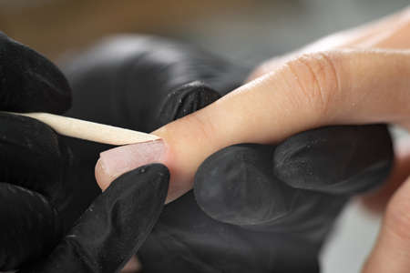 female manicure process. unrecognizable lady doing manicure in spa salon. female beauty and health. The master forms the shape of the cuticles using a bamboo stick close-up.の写真素材