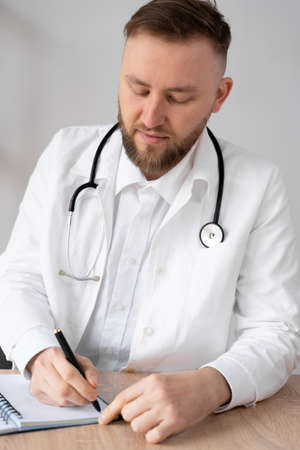 Qualified serious male therapist making notes in a medical journal. Focused young doctor.の写真素材