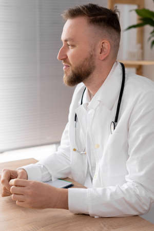 side view of a male doctor in the office working at the table. Serious doctor is waiting for the patient. A portrait of a doctor in a bright office is ready for work. copyspace.の写真素材