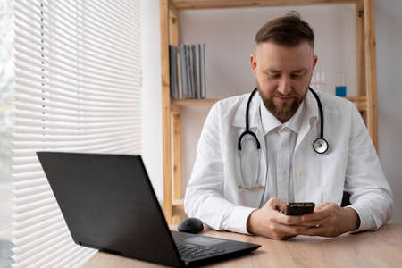 close-up portrait of a doctor he uses a mobile smartphone, works on a laptop in a medical office in a hospital, EHR electronic medical record system, cloud storage technology concept.の写真素材