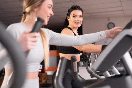 two attractive athletic young women are training together in the gym. Perform exercise on a cardio...