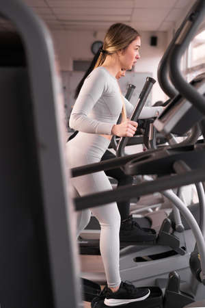 caucasian attractive young athletic woman is training in the gym. Woman exercising on a cardio machineの写真素材