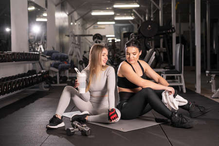 Two beautiful sports girls are sitting on the floor of an industrial gym. They are satisfied with their training program, rest after exercise. copy spaceの写真素材