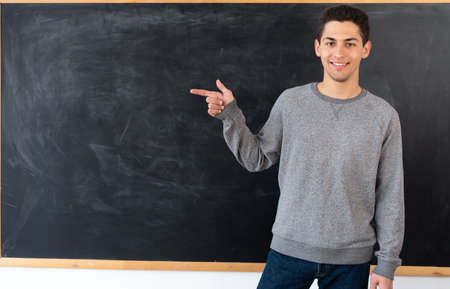 arabic young teacher standing in front of a blank board at the university, smiling student points with his hand at the chalk board with space for text. template for design. education concept.の写真素材