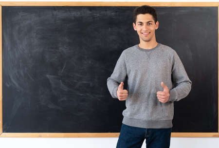Portrait of a young arabic student standing near the blackboard, showing hands class, chalk board in the classroom, man start studying, education conceptの写真素材