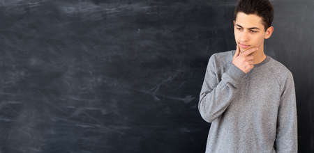 Portrait of thoughtful arabic student or teacher near school blackboard, chalk board background and young male, college concentration problem, space for text, bannerの写真素材