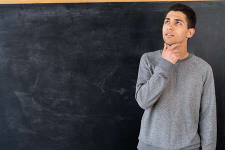 Portrait of focused thinking arabic young teacher near blackboard in classroom, university student chalk board background, education concept, space for text, bannerの写真素材