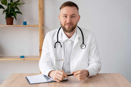 Portrait of male doctor in office working at table. Serious doctor is waiting for the patient. Portrait of a smiling doctor in a bright office. Confident general practitioner ready to go. copyspace.の写真素材