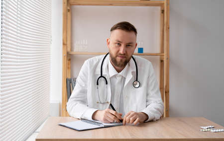 happy young male doctor wears white medical coat and stethoscope looking at camera. Smiling doctor, general practitioner consulting a patient online via video call. Close-up headshot portrait. copyの写真素材