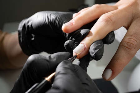 the process of distributing varnish on a nail in a beauty salon close-up. A woman in the salon receives a manicure from a beautician. Transparent nail polish and brush, macro. Shallow depth of fieldの写真素材
